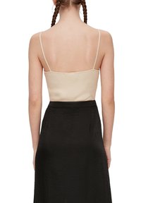 Beige geribbelde tanktop met dunne bandjes, gecombineerd met een zwarte rok. De tanktop heeft een nauwsluitend ontwerp en een gladde textuur.