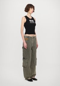 Melna ribota bez piedurknēm topa ar "Moschino Jeans" tekstu, kombinēts ar olīvzaļām cargo biksēm ar lielām sānu kabatām un nodilušu tekstūru.