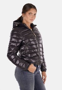 Giacca a vento gonfiata in materiale nero lucido, con zip frontale, cappuccio e polsini a costine. Design a righe orizzontali con tasche laterali.