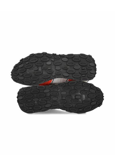 Suole di scarpe in gomma nera con una trama ovale. Fessure visibili e un leggero accento rosso al centro. Design piatto e durevole.