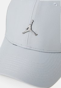 Lys grå baseball cap lavet af tekstureret stof, med et metallisk Jumpman-logo på fronten. Struktureret, seks-panel design med syninger.