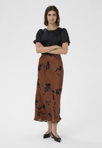 Blouse noire à manches courtes et jupe à imprimé floral marron. La jupe présente un motif floral sombre ; le tissu a une texture lisse et fluide. Ballerines noires à bout pointu.