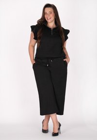 Sort to-delt outfit bestående af en zip-top med flæset ærmer og løstsiddende bukser. Glat tekstur med snoretræk i taljen.