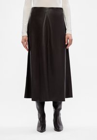 Svart läderkjol i midjelängd med en elegant design, som har en rak skärning, sidofickor och en mjuk textur. Bärs med svarta spetsiga stövlar.