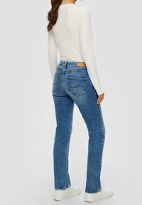 Modré džíny s vysokým pasem a úzkým střihem, s kapsami na zadní straně a texturovanou tkaninou. V kombinaci s bílým topem s dlouhým rukávem a žebrovaným vzorem.