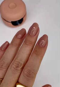 Manicure in gel nudo su cinque unghie, con una finitura lucida. Sullo sfondo, un contenitore rotondo di colore pesca parzialmente aperto che rivela un contenuto nero.