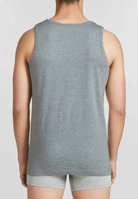Top in cotone grigio senza maniche con scollatura rotonda, mostrato dalla vista posteriore. Il tessuto è morbido e leggero, sovrapposto a pantaloni corti grigio chiaro.