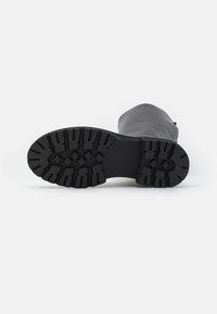 Suela de bota de goma negra con un patrón de dibujo profundo para tracción, presenta una superficie plana y ligera flexibilidad. Acabado liso y mate.