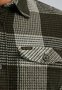 Chemise en flanelle à carreaux verts et blancs avec une poche boutonnée arborant l'étiquette "PME LEGEND", présentant des textures et motifs contrastants.