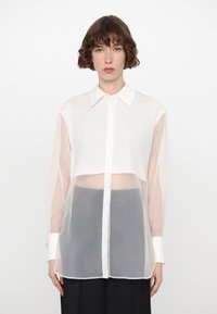 White sheer blouse featuring a cropped design, translucent long sleeves, button-up front, and contrasting white cuffs.