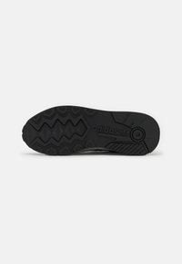 Čierna gumená podrážka topánok s textúrovanými vzormi, obsahujúca logo Adidas a výrazný dezén pre trakciu. Ploské a zaoblené špičky.