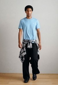 Világoskék, rövid ujjú póló, fekete bőszárú nadrág és fekete-fehér kockás ing, amelyet a derekán kötött össze. Simogató tapintású anyag és laza szabás.