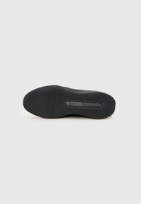 Crna atletska cipela sa potplatom koji ima teksturirani gumeni dizajn sa cik-cak i kružnim uzorcima, te Nike logo u središtu.
