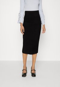 Black fitted midi skirt with a smooth texture, paired with a light blue ribbed top featuring ruched sleeves. Shiny black Mary Jane shoes.