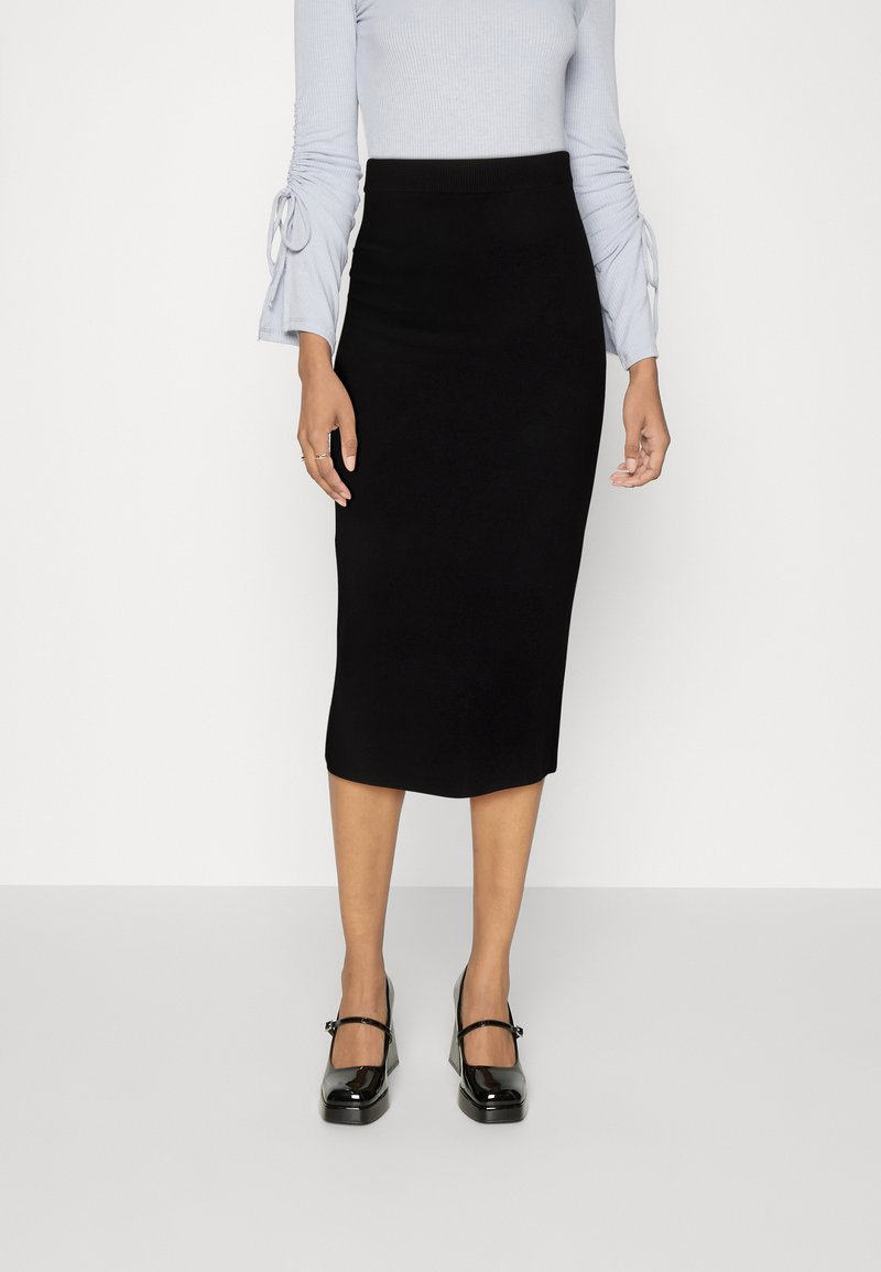 Black fitted midi skirt with a smooth texture, paired with a light blue ribbed top featuring ruched sleeves. Shiny black Mary Jane shoes.