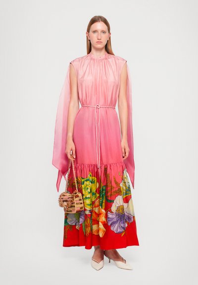 Vestido de seda rosa con un escote fruncido y mangas fluidas, que presenta un estampado floral en colores vibrantes. Acompañado de un pequeño bolso de mimbre y tacones.