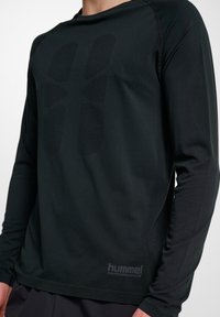 Zwarte lange mouwen sportshirt, gemaakt van rekbare stof, met een gestructureerd logo en patroon op de voorkant en stikseldetails.