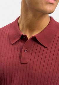 Bordeaux polo skjorta med ribbad textur, kort krage, knappslå med tre knappar och kontrasterande knapppar. Slät tygfinish.