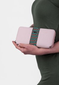 Pink fabric wallet with a zigzag patterned black, teal, and peach band. Rectangular shape, zip closure, held in a hand against a dark background.