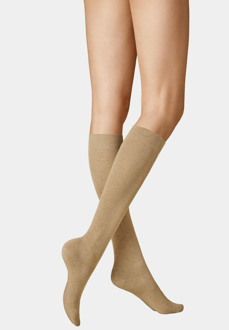 Beige kniehohe Socken aus weichem, strukturiertem Material mit geripptem Bund. Die glatte Oberfläche erstreckt sich über Wade und Fuß, ohne Muster oder Akzente.