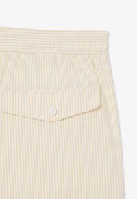 Tissu à rayures verticales jaune clair et blanc avec une ceinture élastique et un détail de poche rabat boutonnée.