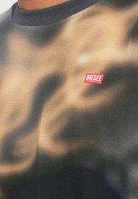 Κοντινό πλάνο σκούρου t-shirt με ανάμεικτα μαύρα και μπεζ σχέδια και μικρό κόκκινο λογότυπο Diesel στο στήθος.