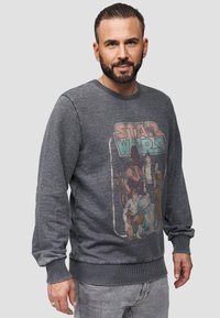 Felpa grigia con maniche lunghe, polsini a coste e colletto rotondo. Presenta una stampa grafica colorata di Star Wars sul davanti.