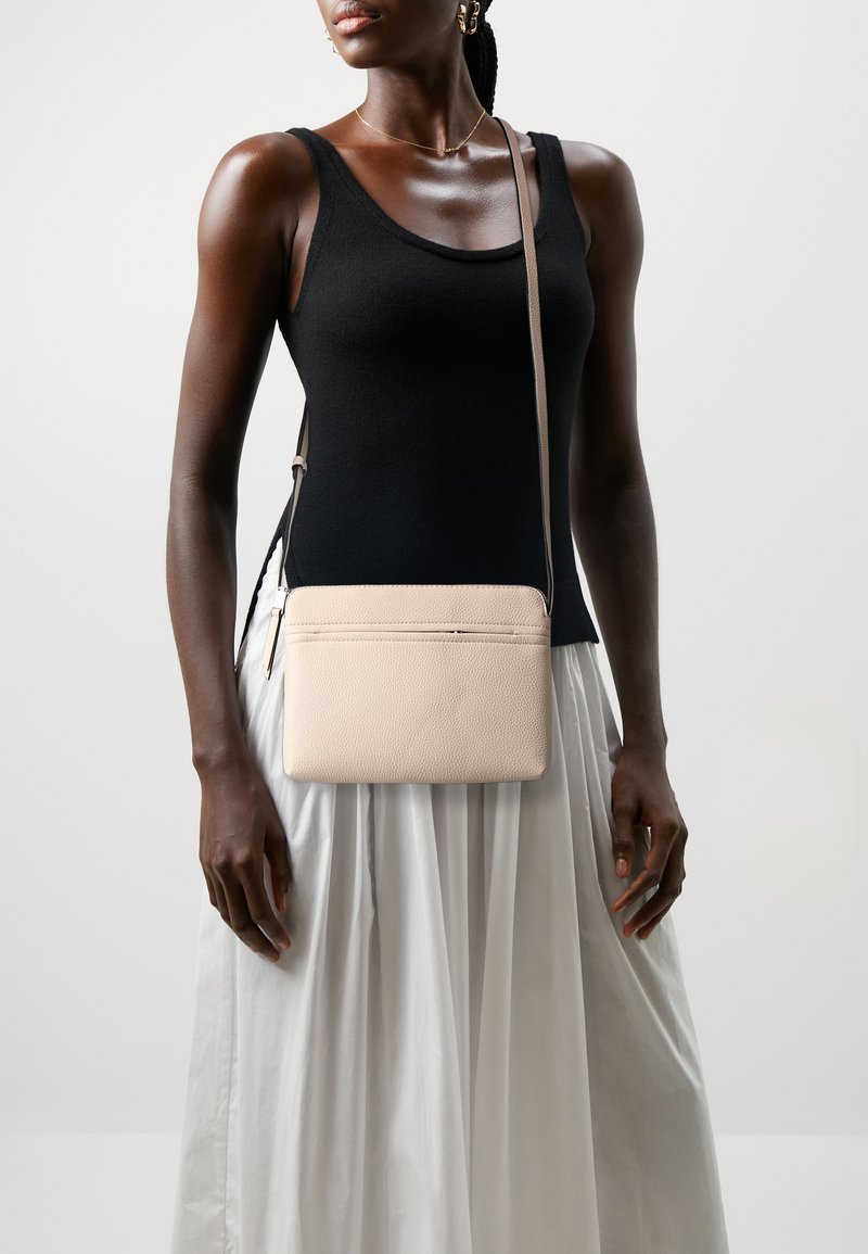 Light pink leather crossbody bag with textured finish, slim rectangular shape, and a front zip pocket. Adjustable strap attached.