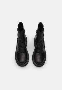 Botas de cuero negro hasta el tobillo con una textura suave, puntera redondeada y paneles laterales elásticos, que cuentan con una suela de goma gruesa y detalles de costura.