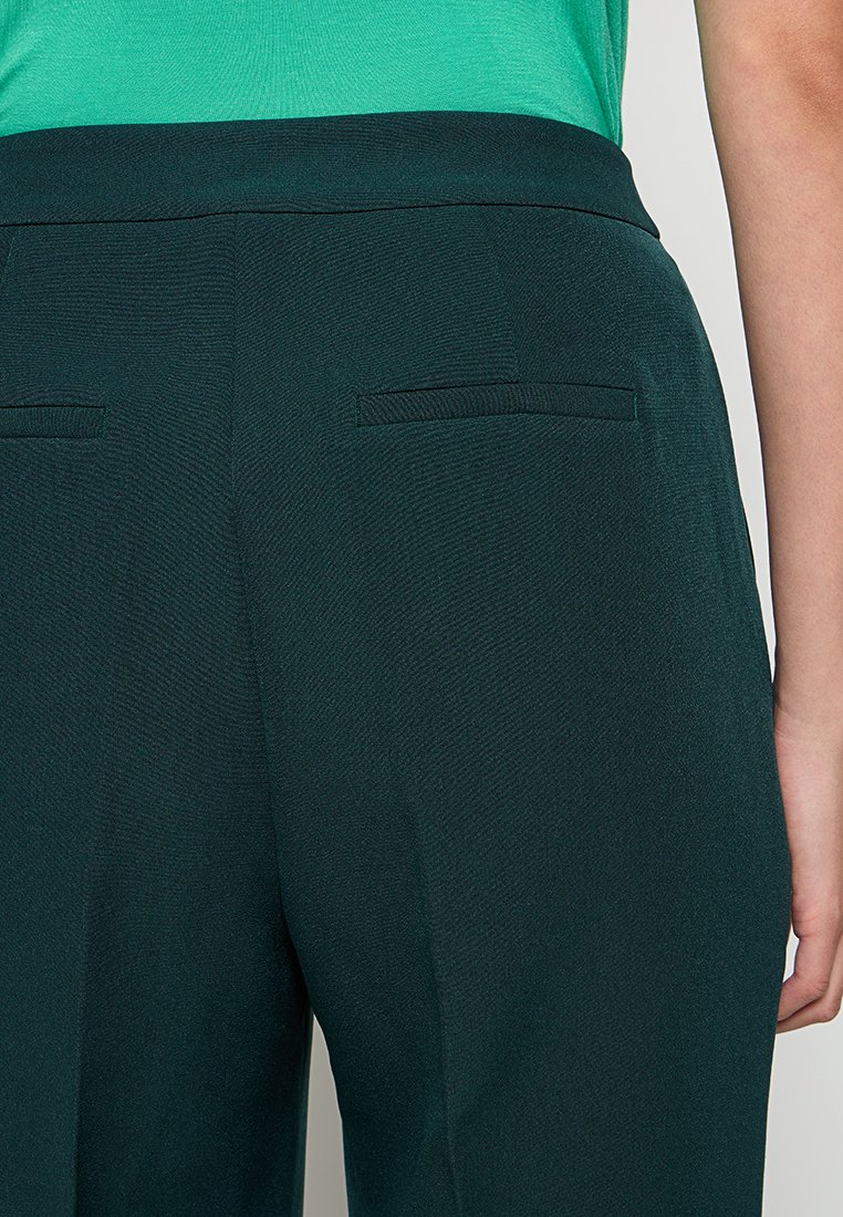 Donkergroene op maat gemaakte broek van een gestructureerde stof. Bevat twee achterzakken met subtiele stikdetails en een soepele tailleband.