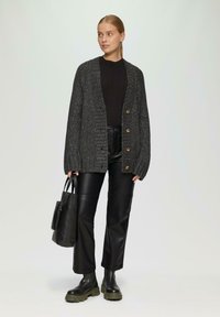 Grijze gebreide cardigan met gouden knopen, gecombineerd met een zwarte geribde top en zwarte leren broek. Gestyled met zwarte legerboots en een tas.