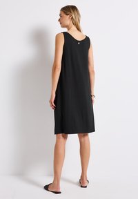 Czarna sukienka bez rękawów z dekoltem w serek, z małym detalem w postaci guzika. Wykonana z miękkiego materiału, ma luźny krój i sięga do połowy łydki.