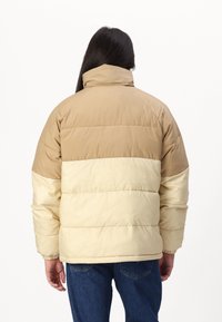 Puffer jacket featuring a tan and cream color block design, with a high collar and ribbed cuffs, made from a smooth, water-resistant material.
