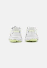 Zapatillas deportivas blancas con un upper texturizado, acentos en amarillo neón y un cuello acolchado. Suela de goma para agarre con un patrón de tracción distintivo.