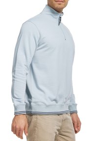 Pull-over bleu clair avec un col montant, une demi-fermeture éclair, des poignets et un ourlet côtelés avec des rayures bleu marine et blanches. Texture de tissu doux.