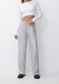 Pantalon large argenté en tissu brillant et texturé avec une taille élastique et un cordon de serrage. Associé à un haut blanc ajusté et court.