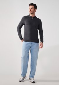 Tmavě šedý polo svetřík s dlouhým rukávem, skloubený se světle modrými džíny a stříbrnými sportovními botami. Polo má límec a knoflíky.