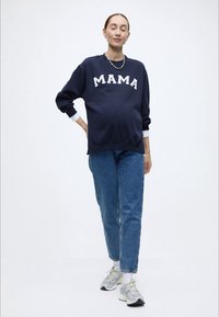 Μπλε φούτερ με λευκά γράμματα "MAMA", συνδυασμένο με ανοιχτόχρωμο τζιν και λευκά αθλητικά παπούτσια. Χαλαρή εφαρμογή και ριμπ μανσέτες.