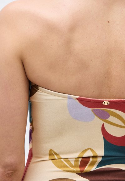 Γυμνή άνω πλάτη και ώμος ενός ατόμου που φοράει τοπ χωρίς τιράντες, πολύχρωμο με αφηρημένα σχέδια σε κόκκινο, μωβ, κίτρινο και μπλε χρώμα.