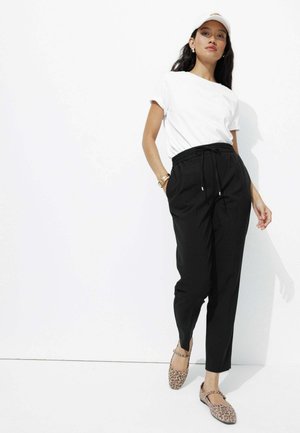 Pantalons noirs fuselés avec taille élastique à cordon, associés à un t-shirt blanc et des ballerines à imprimé animal. Design simple, tissu léger.