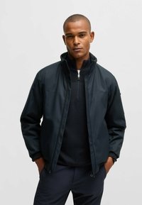 Schwarze leichte Jacke mit hohem Kragen, Reißverschluss und langen Ärmeln; strukturiertes Material; zeichnet sich durch ein minimalistisches Design und seitliche Taschen aus.