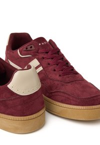 Zapatillas de ante burdeos con acentos beiges, que cuentan con cierre de cordones, suela de goma texturizada y rayas dobles a los lados.