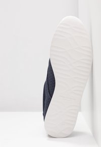 Mörkblå skor med överdel i strukturtyg, vit gummisula med vågmönster och logotyp på innersulan. Storlek 37.