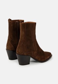 Cizme de gleznă din suede maro închis cu toc bloc, fermoar lateral și detalii cusute vertical pe laturile exterioare.
