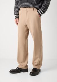 Pantalones beige hechos de una tela suave, con un diseño clásico de pierna recta y bolsillos frontales. Combinados con zapatos de vestir negros.