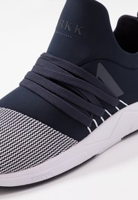 Granatowe buty sportowe z elastycznym materiałem wierzchnim, teksturowanym szarym i białym wzorem na nosku, grubymi granatowymi sznurowadłami oraz białą podeszwą z detalem logo.