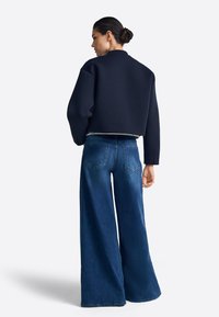 Korte marineblauwe sweatshirts met brede mouwen, gecombineerd met hoog getailleerde, uitlopende blauwe jeans met achterzakken en een vervaagde textuur.