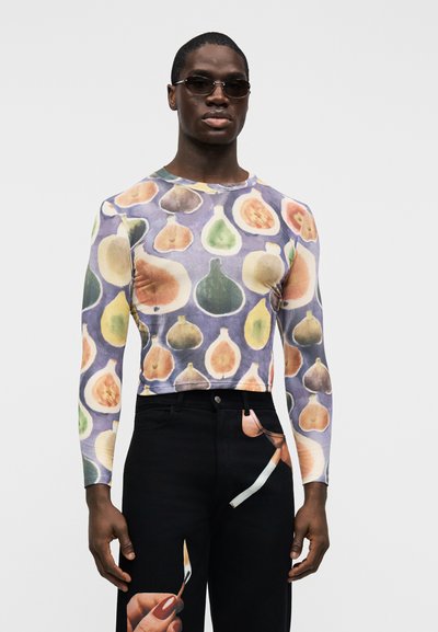 Košeľa s dlhým rukávom s ovocným vzorom v tlmených farbách na svetlej tkanine; v kombinácii s čiernymi džínsami s grafikou ruky a štetca.