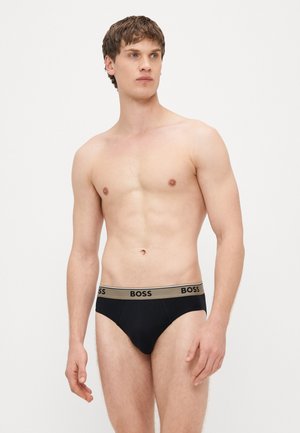 Cuecas pretas com uma cintura bege que apresenta o logo "BOSS". O tecido parece liso e elástico, concebido para o conforto.