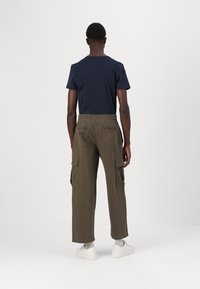 Navy cotton t-shirt with a round neckline, paired with olive green cargo pants featuring multiple pockets and an elastic waistband. White sneakers.